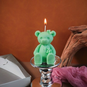 Detail of mint green bear candle with bow and heart necklace lit on a silver holder