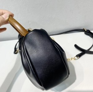 Detail of black leather cloud bag with light brown wooden handle and gold hardware