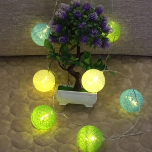 Detail of colorful cotton ball string lights draped on a potted plant for room decor