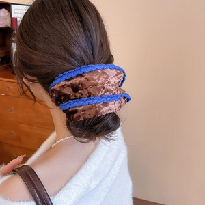 Close-up of a large velvet hair scrunchie with blue woven edges worn on a bun