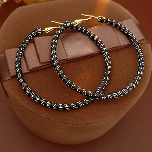 Macro shot of large black leather hoop earrings with white NICE letter patterns and gold posts