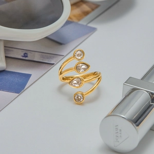 Spiral gold titanium ring with round and pear-cut zircon stones on a stylish desk setting
