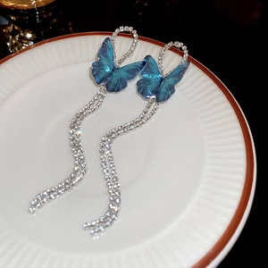 Détail de boucles d'oreilles papillon bleues avec pompons et strass sur plat blanc