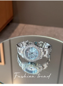 Macro view of a silver quartz watch with a diamond bezel and light blue dial on a mirror