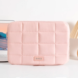 Pink quilted laptop sleeve with square stitching and leather logo on a cozy desk setup