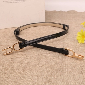 Minimalist black patent leather skinny belt with gold buckle on linen background