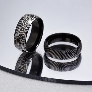 Close-up of black titanium rings featuring Damascus steel pattern and mirror reflection