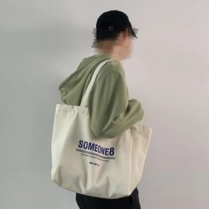Close-up of large canvas tote bag with letter print and shoulder strap on model