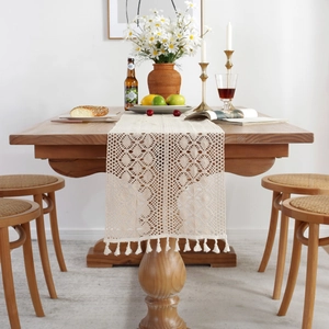 Detailed close-up of beige crochet table runner with fringe on a rustic wooden dining table