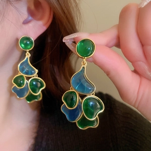 Close-up of vintage gold tassel earrings featuring green and blue tiered gemstones