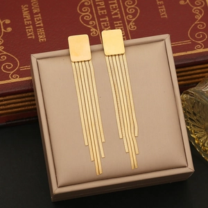 Detailed view of long gold snake chain tassel earrings on a beige leather jewelry box