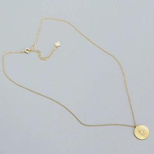 Detail of golden coin necklace with snake engraving and sunburst texture on a thin chain