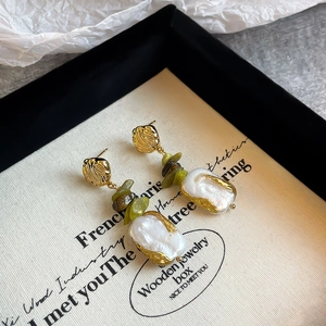 Macro detail of baroque pearl earrings with green stone accents in a luxury jewelry box