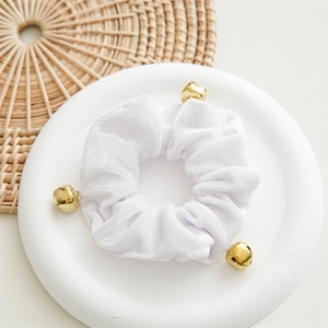 Close-up of white velvet scrunchie featuring three small gold bells on a woven base