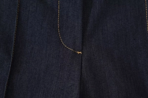 Détail du tissu denim bleu foncé montrant les coutures orange et la texture sergée