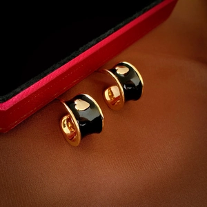 Macro detail of golden C-shaped hoop earrings with black enamel and a small heart design