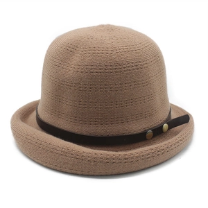 Detail of a brown knit basin hat featuring a leather strap and bronze metal buckles