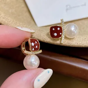 Close-up of 18K gold earrings with red polka dot enamel, cubic zirconia and white pearls