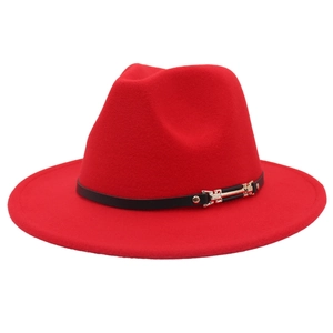 Détail d'un chapeau fedora rouge avec bande en cuir noir et boucle dorée sur fond blanc
