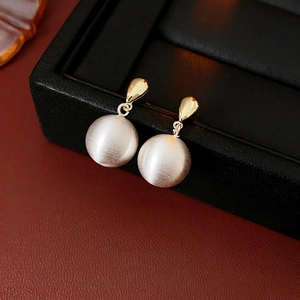 Boucles d'oreilles gouttes dorées avec sphères en métal mat sur présentoir en cuir