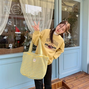 Outdoor shot of a plush striped tote bag held by a model in a yellow graphic sweatshirt
