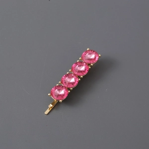 Close-up of golden hair clip set with four faceted round pink crystals on grey backdrop
