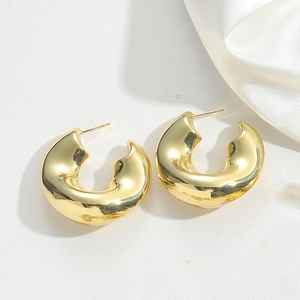 Macro detail of chunky gold C-shaped hoop earrings on elegant white textured surface