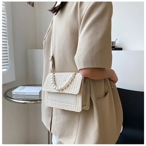 Detail of ivory woven bag featuring pearl handle, leather flap, and gold hardware accents