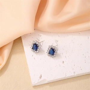 Macro detail of silver bow stud earring with rectangular blue zircon and peach silk background