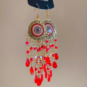 Detail of bohemian gold leaf earrings with intricate red bead tassels and hollow metal discs