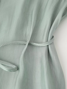 Detail view of light green satin fabric showing the silky texture and waist tie design