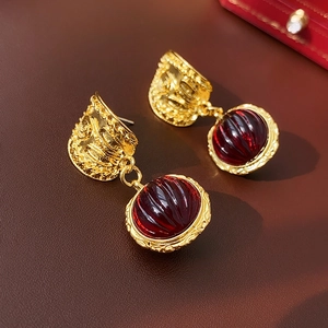 Vintage style gold earrings with dark red beads on a brown leather background