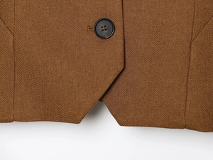 Close-up detail of caramel linen vest hem showing fabric texture and single black button