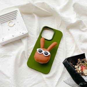 Green silicone phone case with a 3D brown plush rabbit wearing sunglasses on a white tray
