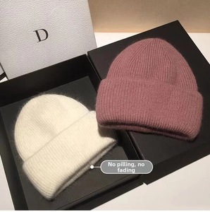 Detailed texture of rabbit fur knit beanies in cream and dusty pink inside a gift box
