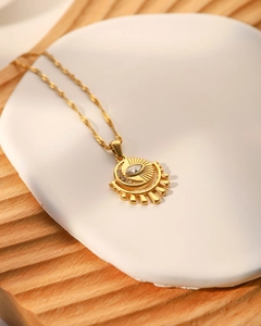 Detail of gold evil eye sun pendant with zircon on water wave chain necklace