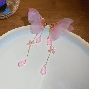 Detail of butterfly tassel earrings with pink gauze wings and flower charms on a ceramic plate