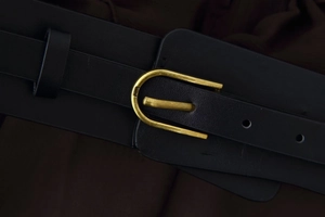 Close-up of black leather belt with a golden metal U-shaped buckle and fine stitching