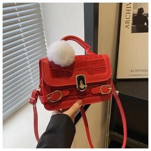 Detail einer roten Handtasche mit Krokoprägung, Plüschanhänger und goldenem Verschluss
