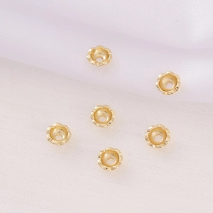 Detail view of six golden floral metal spacers with central holes on white silk background