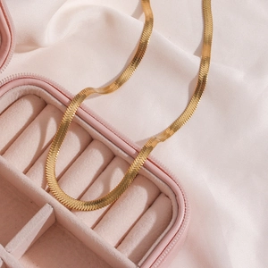 Flat snake bone anklet in 18K gold finish resting on pink velvet box with silk fabric
