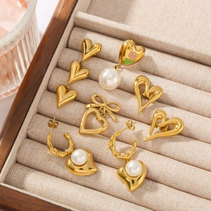 Set of four unique gold-plated heart earrings with pearls and tassels on beige velvet tray