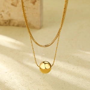Double-layered gold stainless steel necklace with a polished sphere pendant on a stone base
