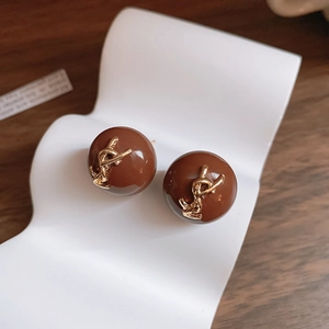 Détail de boucles d'oreilles rondes en résine marron avec logo en métal doré