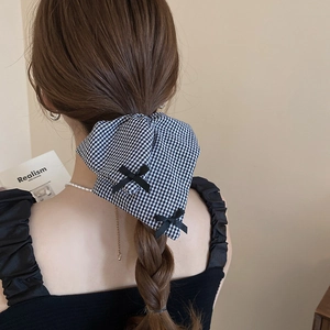 Detail showing oversized black and white plaid bow hair accessory on braided hair
