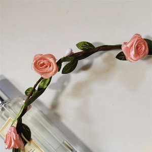 Close-up of pink fabric roses and green leaves on a brown vine headband
