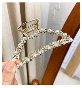 Detailed close-up of a golden metal hair claw clip with inlaid pearls and rhinestones