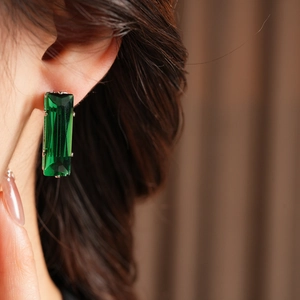 Close-up of a model wearing rectangular emerald green drop earrings with silver pins