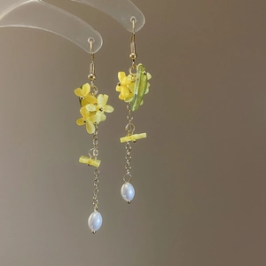 Detail of long tassel earrings featuring yellow flowers and pearl pendants on gold chains