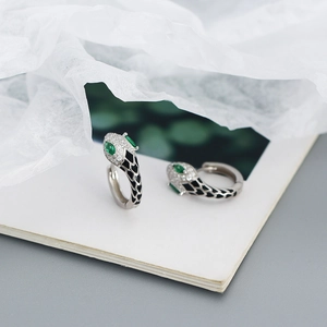 Macro shot of silver snake earrings with green gem eyes and black enamel pattern details